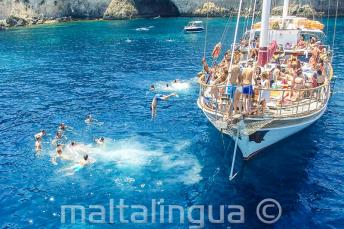 Taal studenten springen van een boot in Crystal Bay, Comino.